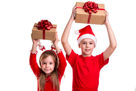 Concept: Christmas or Happy New Year holiday. Cheerful boy with santa hat on his head and a girl with deer horns, holding the gift boxes over their headsの写真素材