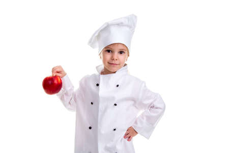 Serious chef girl in a cap cook uniform, holding with one hand on the red apple tail. Another hand is on the waist. Human emotions, facial expression feeling, attitudeの写真素材