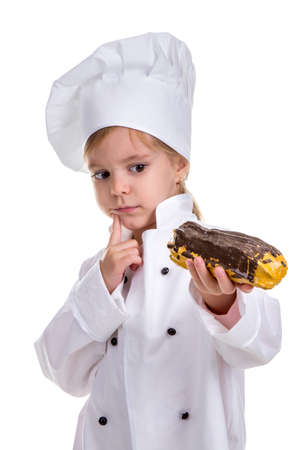 Pensive serious chef girl in a cap cook uniform, appraising the eclair. Looking at it. Portrait imageの写真素材