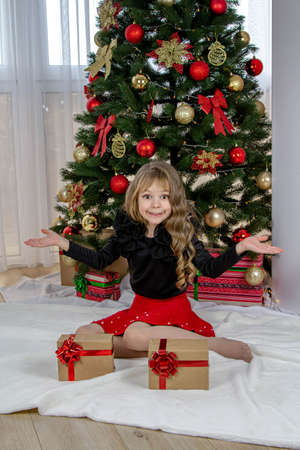 A beautiful little girl stands before the choice of a small or large gift for the New Year and Christmas. The girl decides which gift to chooseの写真素材