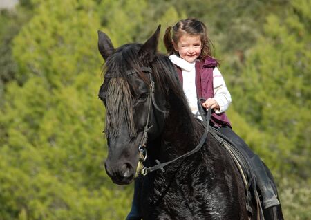 little smiling girl on her black stallion. focus on the childの写真素材