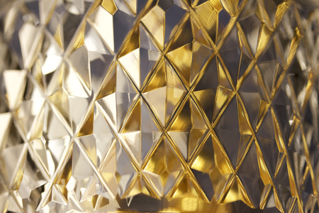 Macro view of beautiful lead crystal glass with diamond cut facets reflecting brilliant gold and silver colorの写真素材