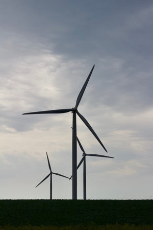 Silhouette of giant wind turbines on an agricultural field with blue sky