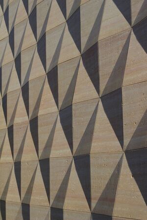 Exterior concrete wall texture with geometric shapes that are enhanced by late day sun shadows (angle view)の写真素材