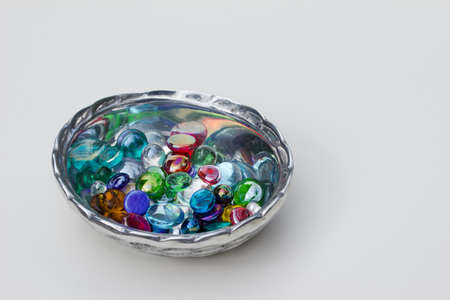 Close up abstract view of a small silver metal bowl containing dragon tears and glass stones on white backgroundの写真素材
