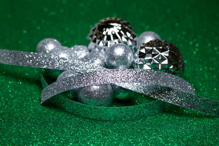 Close up abstract defocused view of silver glitter ornamental Christmas baubles and ribbon, on glittering green background with copy spaceの写真素材