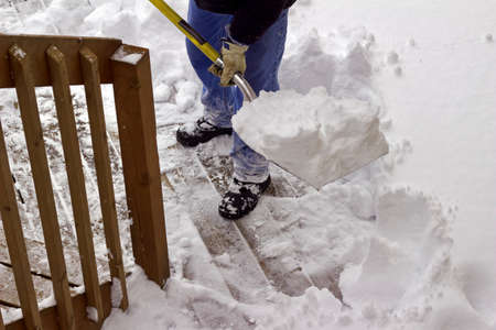 Close up view of an unseen person who is shoveling snow off a wooden deck surfaceの写真素材