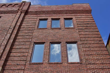 Upward view of a beautiful vintage brown brick wall building with large windows reflecting blue skyの写真素材