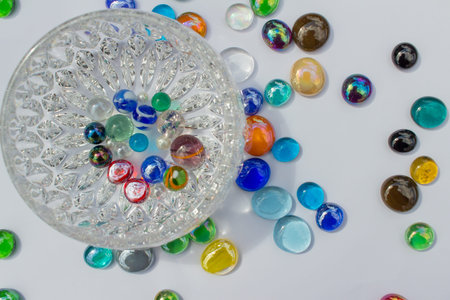 Modern crystal glass bowl surrounded by colorful glass bead dragon tears on white background with copy space