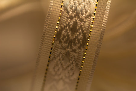 Full frame macro abstract texture view of shimmering silvery white brocade design fabric ribbon with golden accent stitching, on white backgroundの写真素材