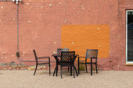 Abstract texture background of an outdoor dining table and chairs along an old deteriorating rosy brown and orange painted brick wall with a rugged shabby chic appearanceの写真素材