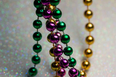 Macro full frame abstract texture view of traditional Mardi Gras bead necklaces (in green, gold, and purple) arranged on a sparkling white glitter backgroundの写真素材