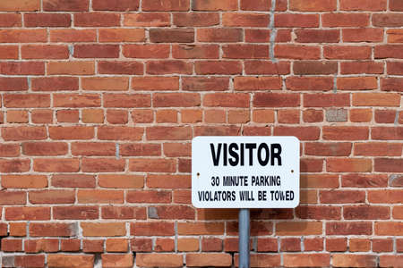 Full frame texture background of a grungy old deteriorating reddish brown clay brick wall, in common bond brickwork pattern, with view of a visitor parking signの写真素材