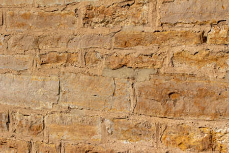 Antique golden brown color natural stone wall background with worn texture in full sunlight, with copy spaceの写真素材