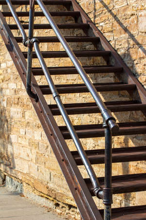 Sturdy metal fire escape staircase along an old white rough textured stone wall background, in full sunlight with copy spaceの写真素材