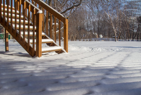 Outdoor view of fresh snow texture designs on a wooden deck and staircase, in winter with natural...