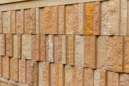 This image shows a modern style rough textured limestone brick wall background with attractive vertical aligned natural kasota stone blocks in varying widths and shades of light brown.の写真素材