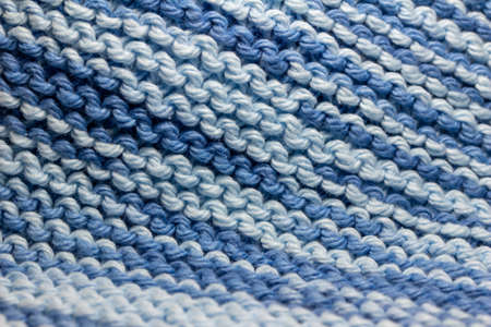 This image shows a macro abstract texture background of a hand-knitted yarn swatch in a basic garter stitch, in varying striated shades of blue and white.の写真素材