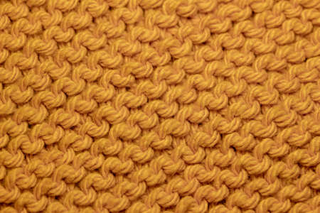 This image shows a macro abstract background of hand-knitted yarn fabric texture with a garter stitch pattern, in the color of golden curry orange.の写真素材