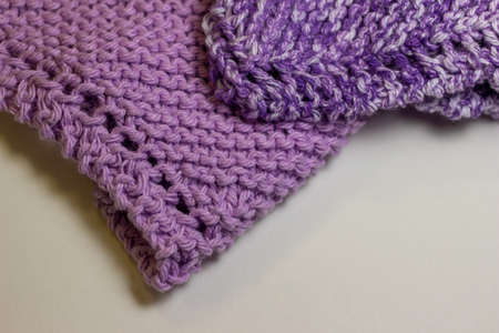 This image shows a macro abstract texture background of hand-knitted yarn cloth in a common garter stitch, in varying shades of purple and white.の写真素材