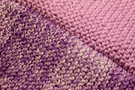 This image shows a macro abstract texture background of hand-knitted yarn cloth in a common garter stitch, in varying shades of purple and white.の写真素材