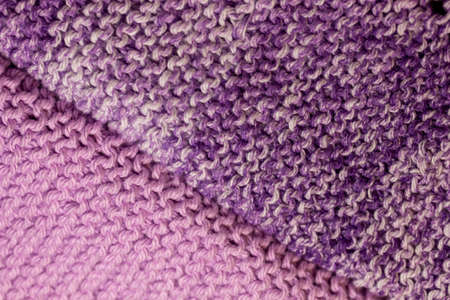 This image shows a macro abstract texture background of hand-knitted yarn cloth in a common garter stitch, in varying shades of purple and white.の写真素材