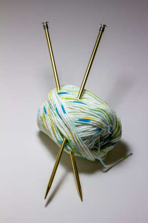 This image shows a close-up studio shot view of a small skein of white, blue, and green cotton yarn and a pair of metal knitting needles.の写真素材