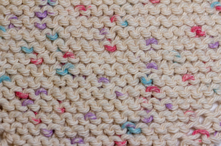 This image shows a close-up abstract view of hand knitted cotton yarn cloth in a simple garter stitch, in a beige color with scattered colorful speckles.の写真素材