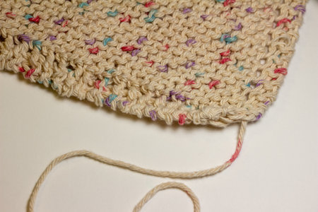 This image shows a close-up abstract view of a hand knitted cotton yarn wash cloth in a simple garter stitch, in a beige color with scattered colorful speckles.の写真素材