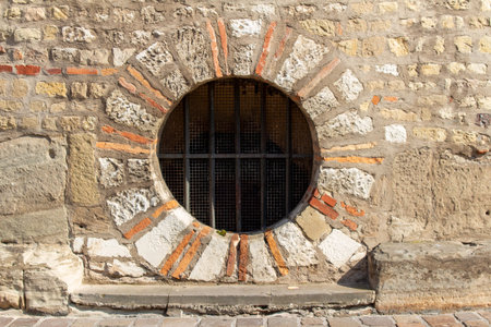 This image shows a full frame texture background of a weathered medieval stone and brick wall with a round basement portal window.の写真素材