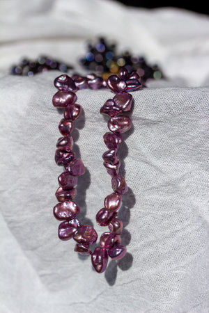 Macro abstract texture background of a deep pink color natural baroque pearl necklace with natural imperfections, on a white cloth surface.の写真素材
