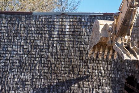 Close up view of an old abandoned barn building being demolished with a heavy equipment excavatorの写真素材