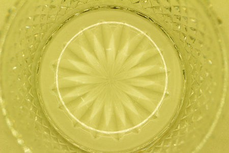 Macro abstract texture background of a round translucent crystal glass surface with a starburst design surrounded by diamond cuts, in the color of translucent yellowの写真素材