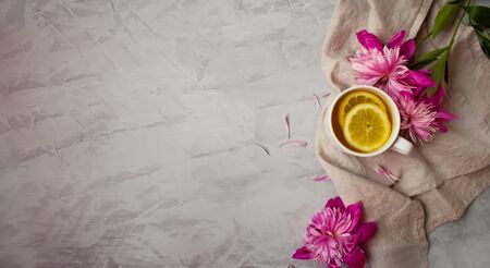 Top view of a warm cup of tea with vibrant pink flowers on grey surface.の写真素材
