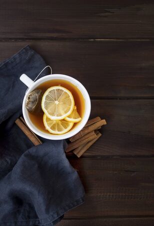 Warm cup of tea with fresh sliced lemon and cinnamon on black napkin on wooden background.の写真素材