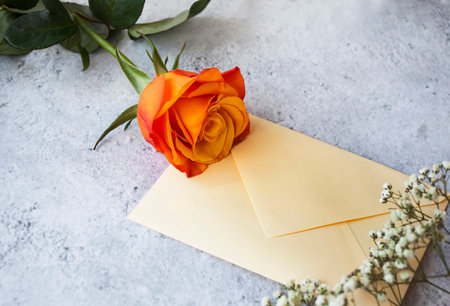 Vibrant yellow-orange rose with a letter and white flowers on grey surface.の写真素材
