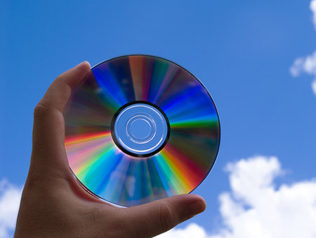 a dvd/cd held by hand against a blue sky