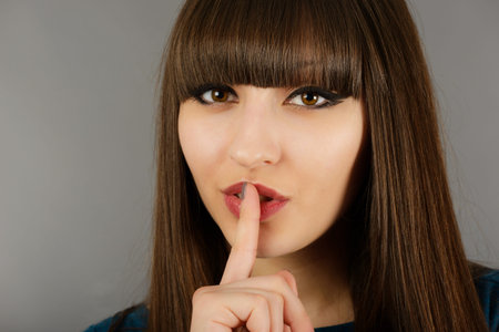 Closeup of young businesswoman making silence sign isolated on gray  background