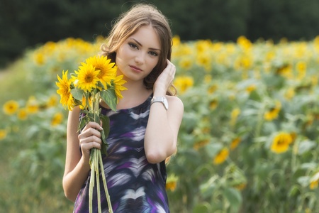 young beautiful woman on blooming sunflower field in summerの写真素材