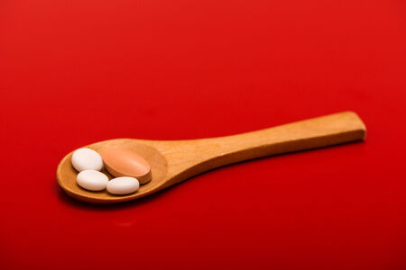 white pills on wooden spoon isolated on red backgroundの写真素材