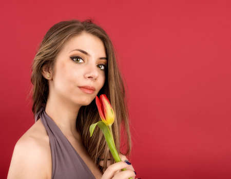 Teenage girl posing with tulip in hands on red backgroundの写真素材