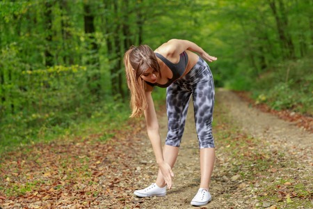 Beautiful young woman doing stretching exercise on road forestの写真素材