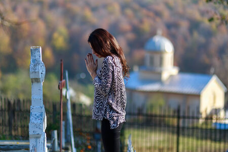 young woman prays in front of a cross in the cemeterの写真素材
