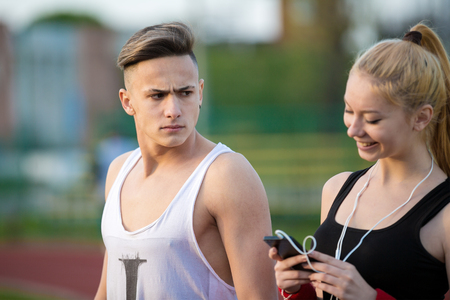 jealous worried man peering over the shoulder of his girlfriend while she is talking on the phone smilingの写真素材