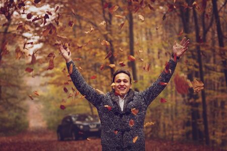 Outdoors portrait of happy young man standing in autumn park at treeの写真素材