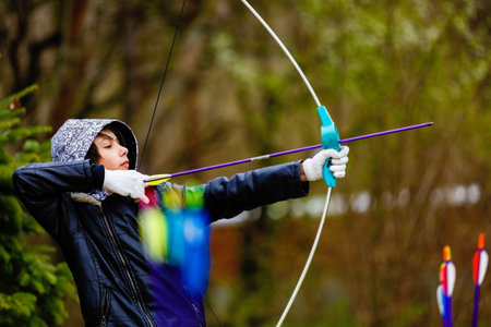 Boy archer shooting with his bow at an outdoor archery range