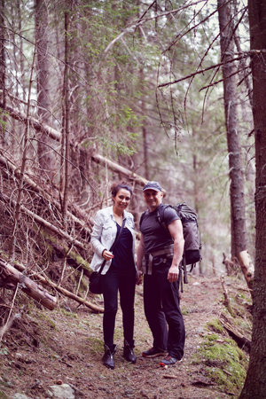 A woman and a man are trekking in the forested mountain