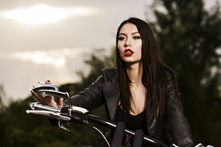 vintage image of a beautiful woman sitting on a motorcycle and smokesの写真素材