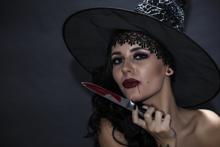 closeup portrait of woman with bloody knife in her hand in the darkの写真素材