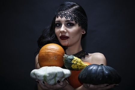Portrait of a gorgeous brunette with a hat and pumpkin over black background. Halloween.の写真素材